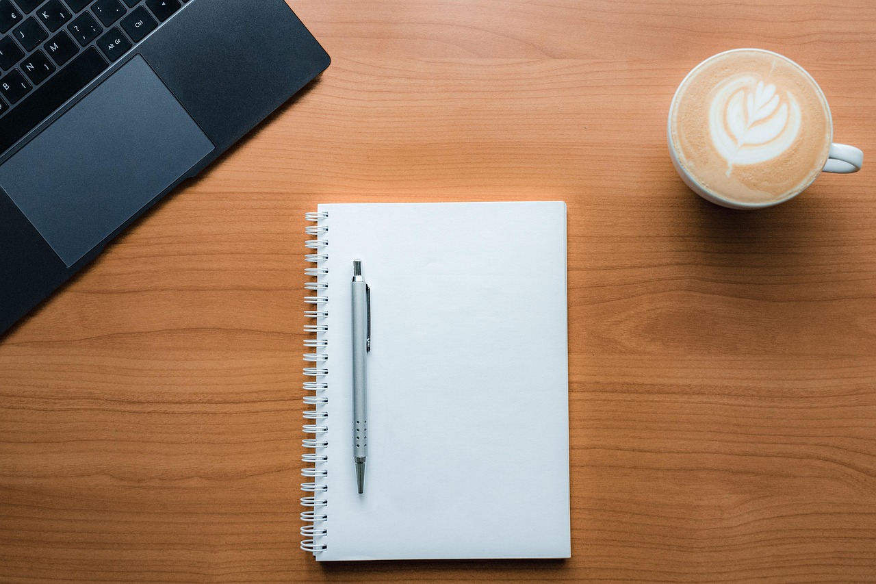 Notebook, caderno e café na mesa de um revisor de texto em trabalho remoto